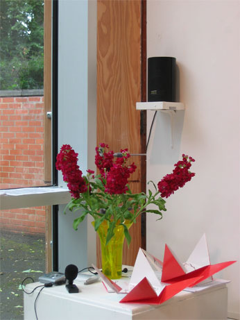 interior shot of gallery with speaker, vase of plowers and origame CD covers open on plynth